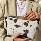 Woman opening the black brown cow print makeup bag to take out a perfume bottle