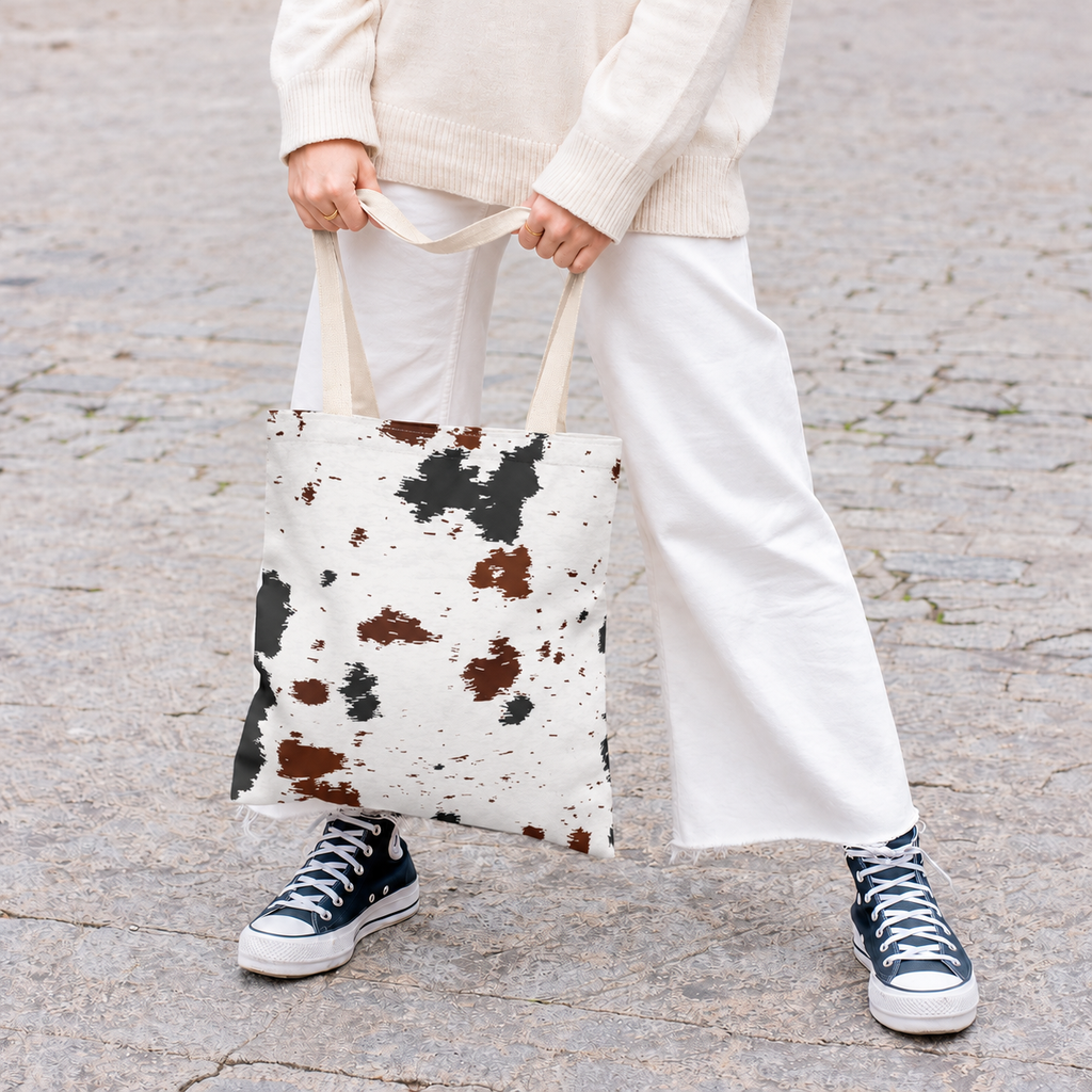 Woman holding the black and brown cow print tote bag in front of her on a street
