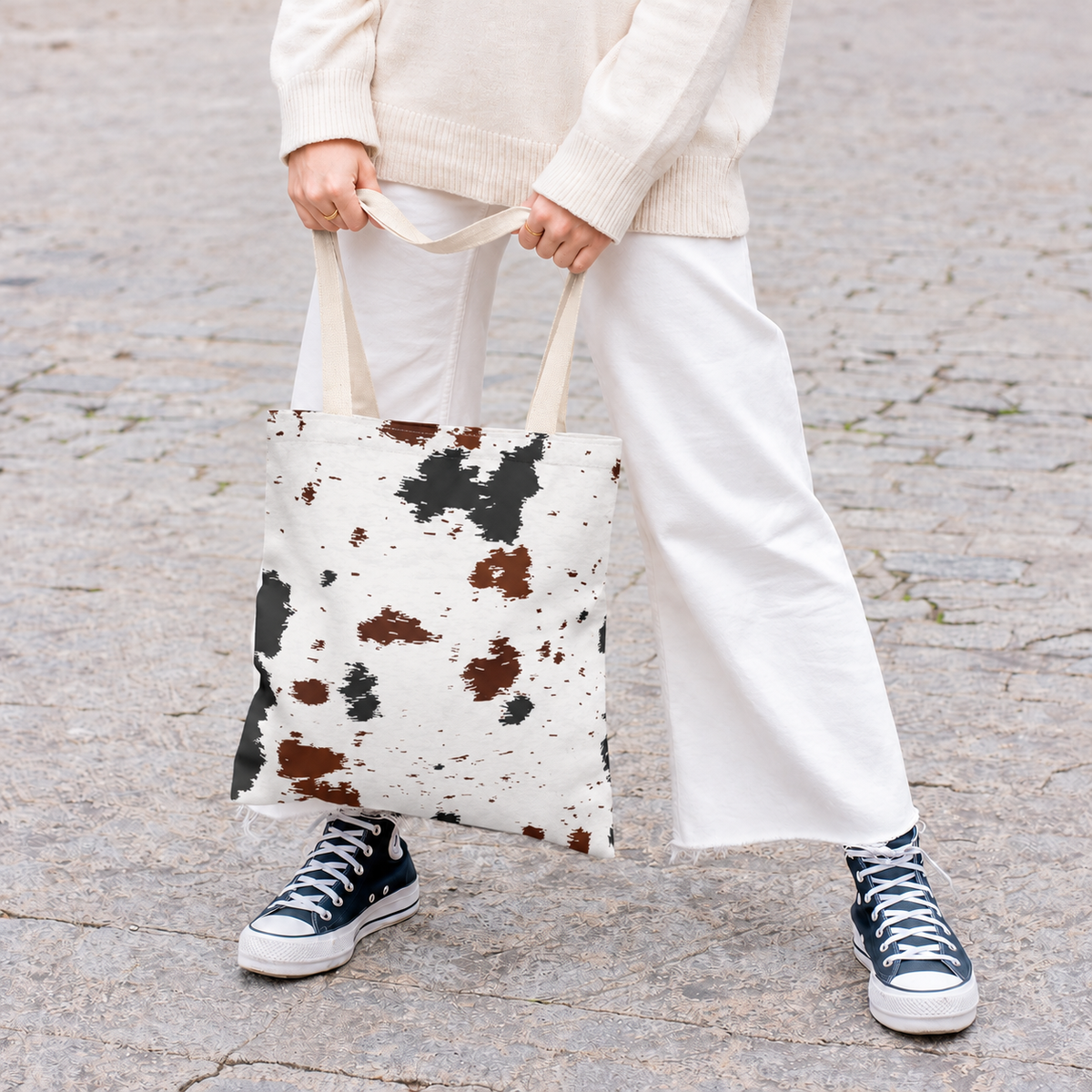 Woman holding the black and brown cow print tote bag in front of her on a street