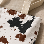 Close-up of the black and brown cow print spots and cream handle of the tote bag