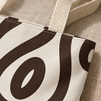 Close-up of the black abstract loop print on cream and the beige handle of the tote bag