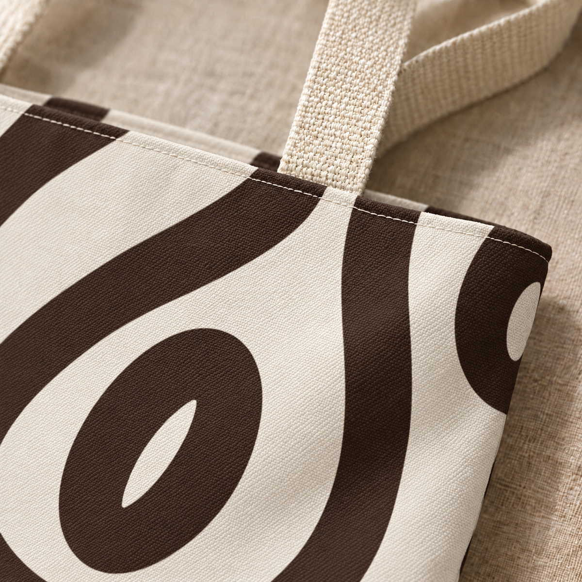 Close-up of the black abstract loop print on cream and the beige handle of the tote bag
