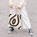 Woman in white trousers holding the black cream abstract tote bag by the handles