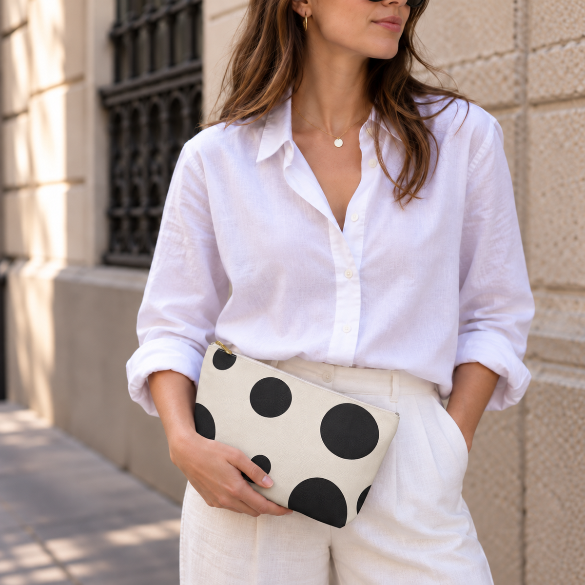 Woman in a white shirt holding the black cream polka dot makeup bag at her hip