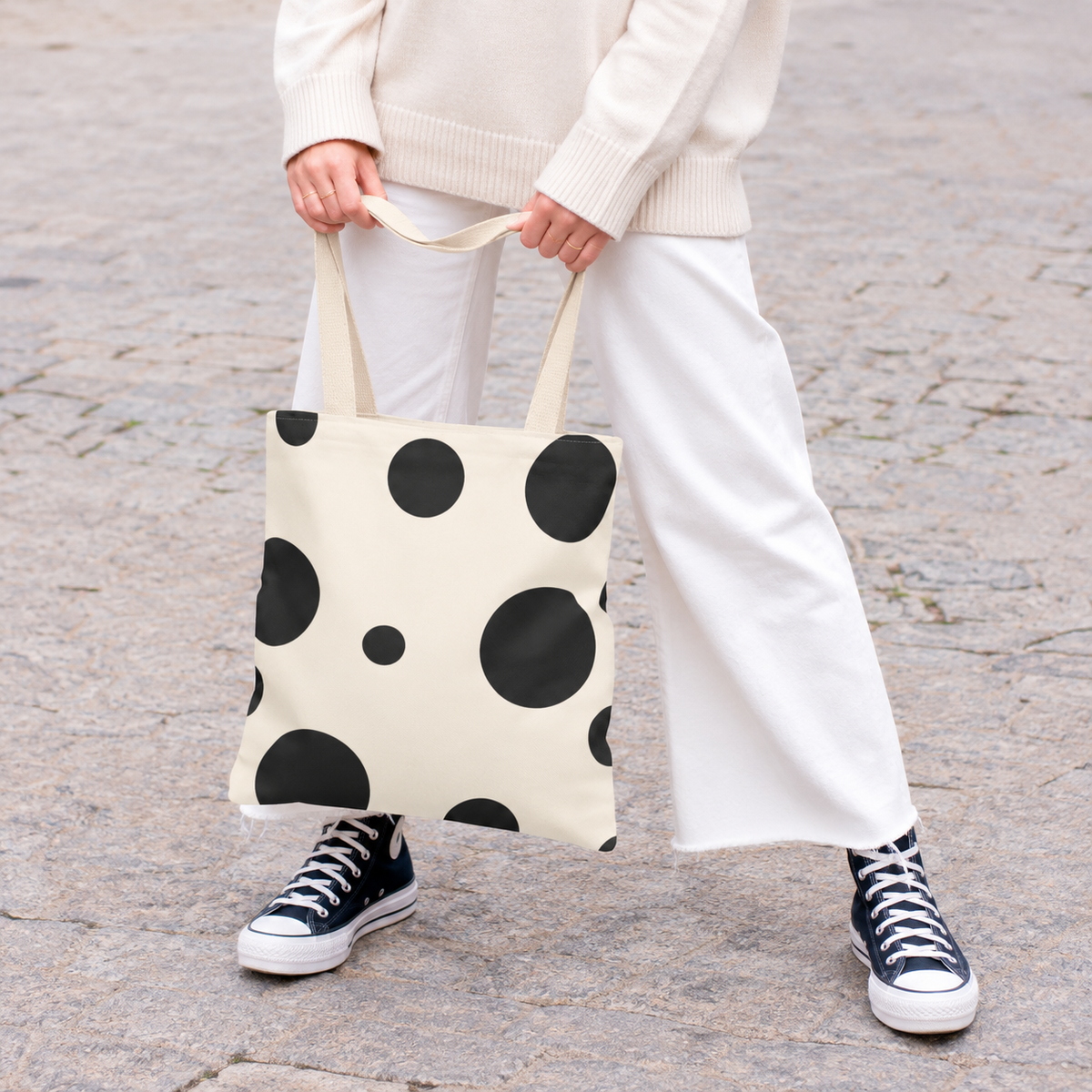 Woman holding the black and cream polka dot tote bag in front of her on a street