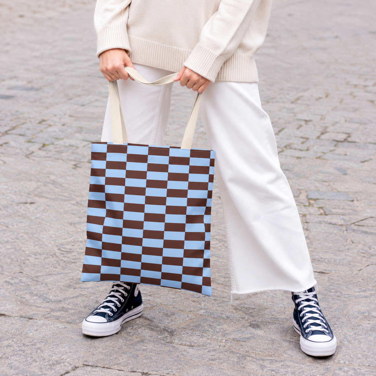 Woman in white trousers holding the blue brown brick tote bag by the handles