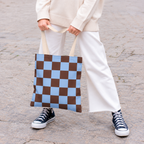 Woman in white trousers holding the blue brown checkered tote bag by the handles