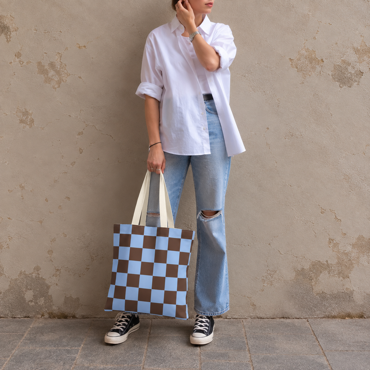 Woman in white shirt and jeans standing with the blue brown checkered tote bag