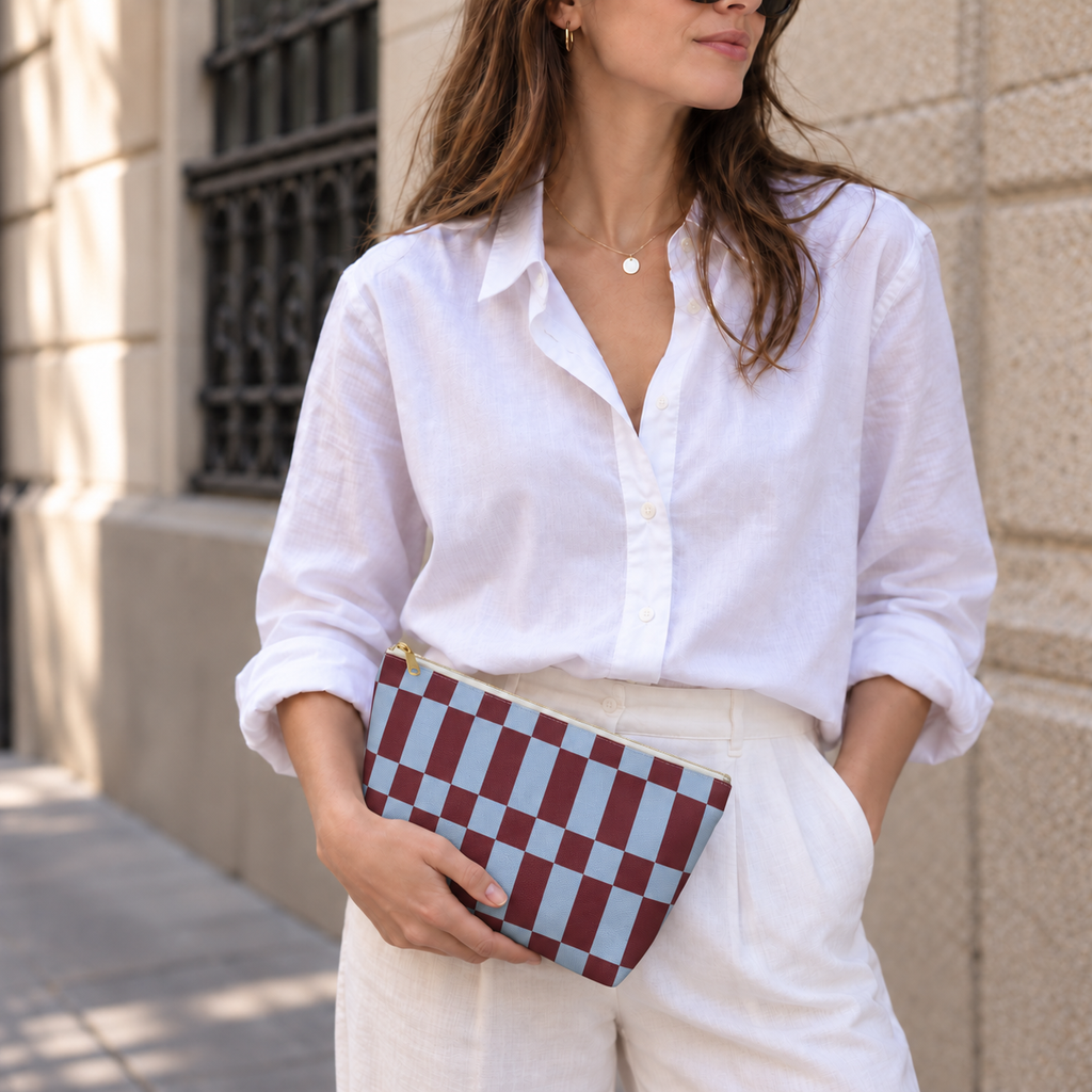 Woman in a white shirt holding the blue burgundy checkerboard makeup bag as a clutch