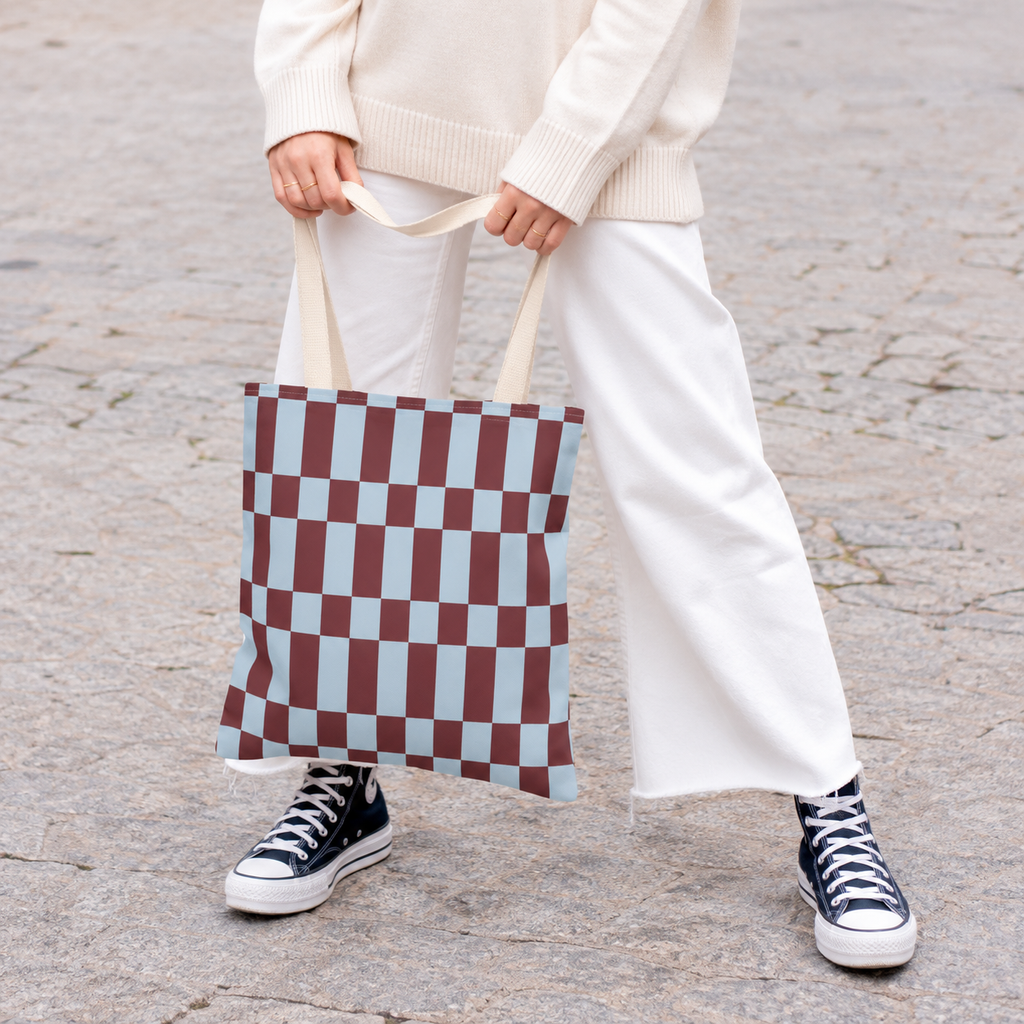 Woman in white trousers holding the blue burgundy checkerboard tote bag by its handles