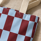 Close-up of the pale blue and burgundy checks and the beige handle on the checkerboard tote bag