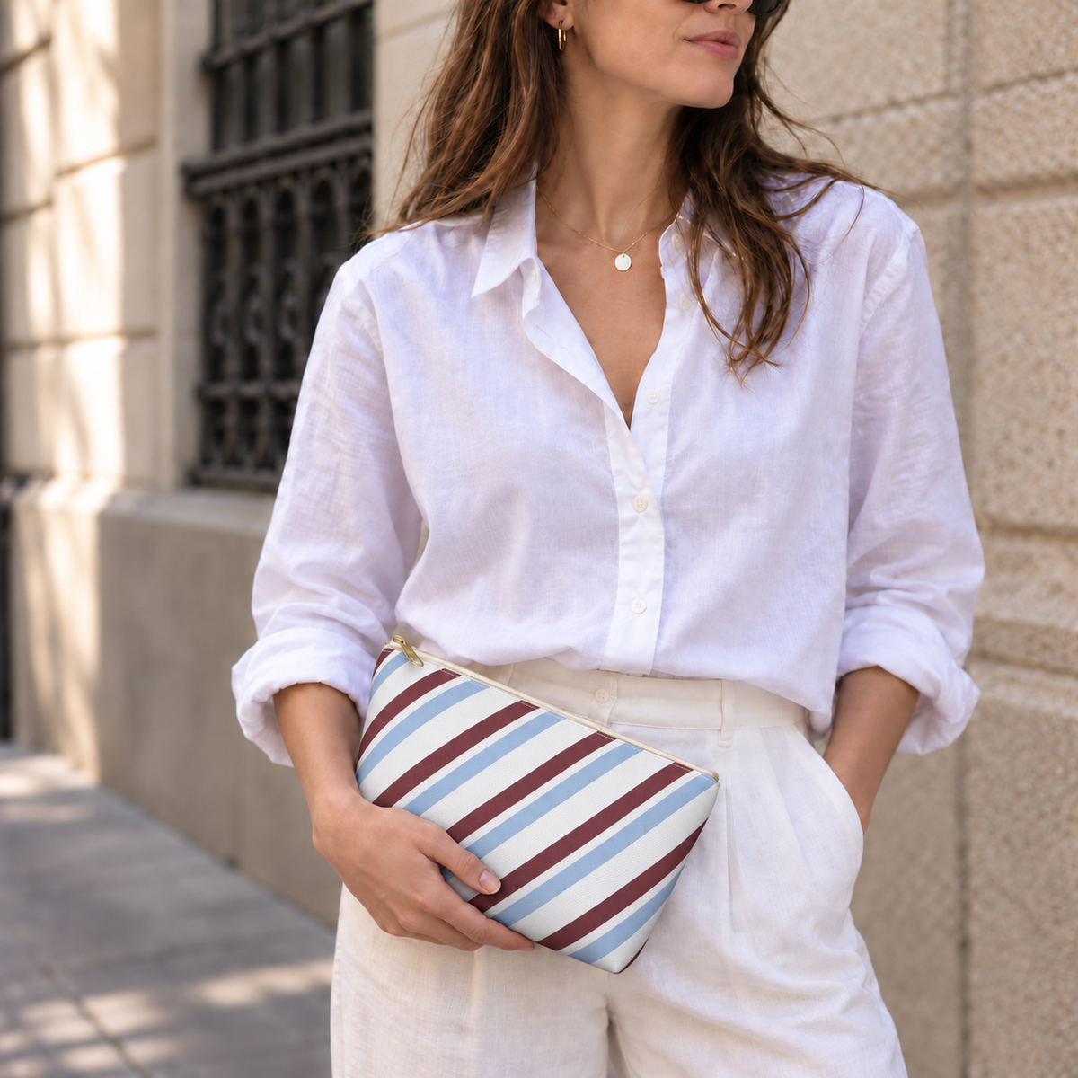 Woman in a white shirt holding the blue burgundy diagonal striped makeup bag as a clutch
