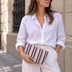 Woman in a white shirt holding the blue burgundy dot striped makeup bag as a clutch
