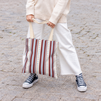 Woman in white trousers holding the blue burgundy dot striped tote bag by its handles