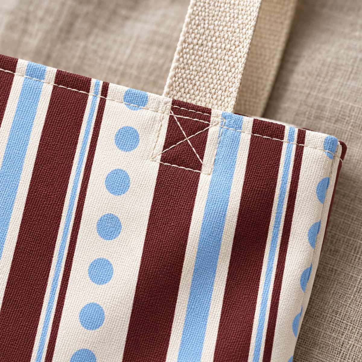 Close-up of the burgundy and light blue stripes with blue dots and the beige handle on the dot striped tote bag