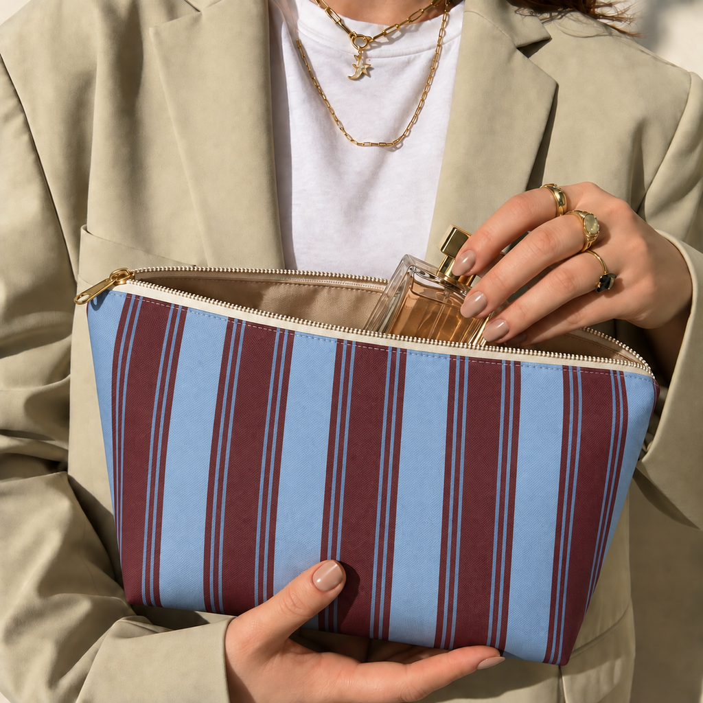 Hands holding the blue burgundy striped makeup bag while taking out a perfume bottle