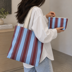 Woman with a striped tote bag on her shoulder holding the matching striped makeup bag