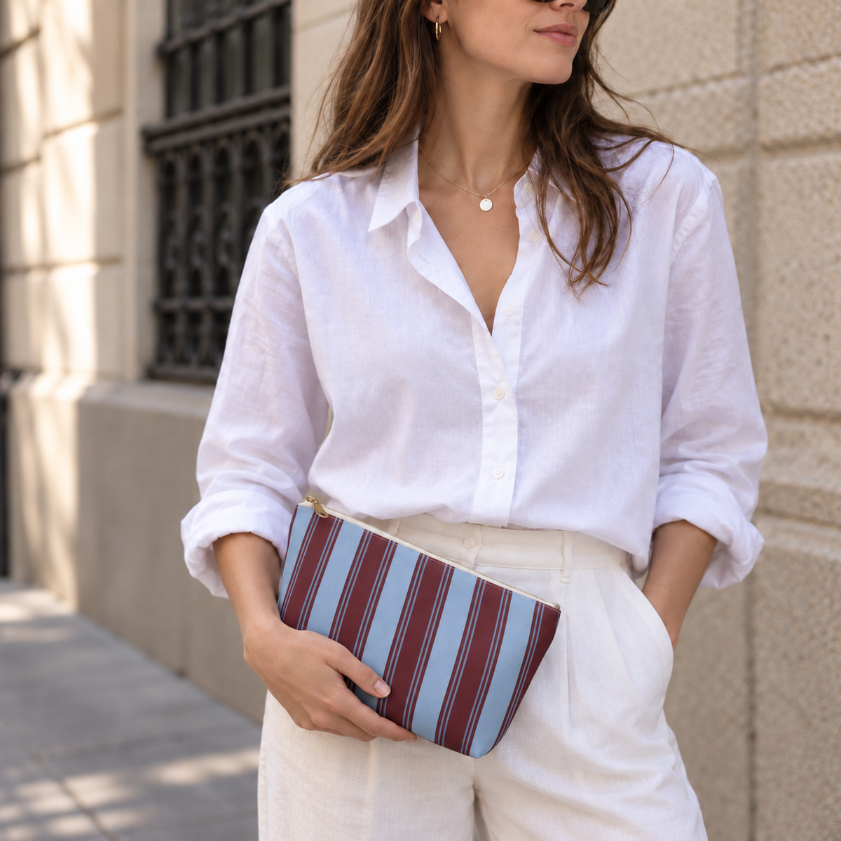 Woman in a white shirt holding the striped makeup bag at her waist
