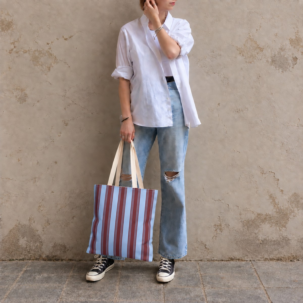 Woman in a white shirt and jeans holding the blue burgundy striped tote bag by its handles