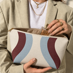 Model opening the wavy makeup bag in blue and burgundy to take out a perfume bottle