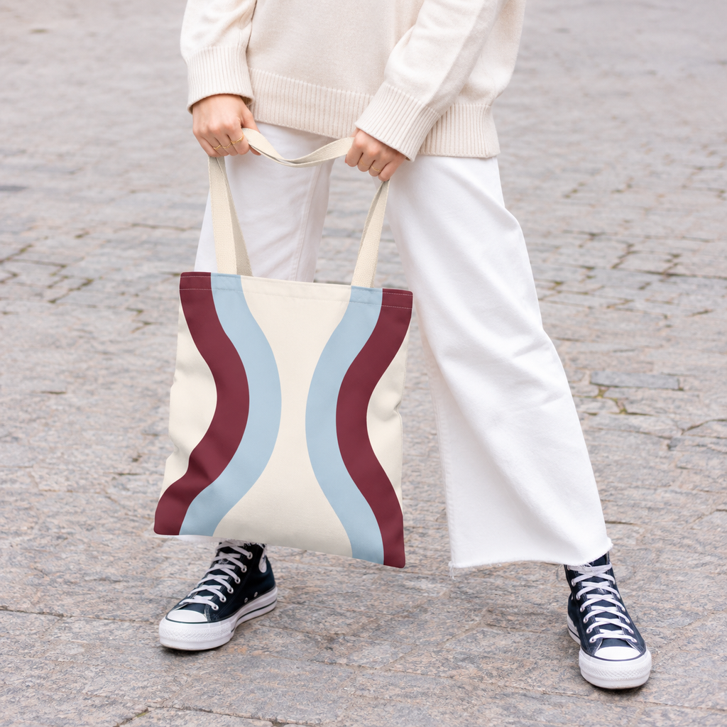 Model in white trousers holding the wavy tote bag in sky blue and burgundy