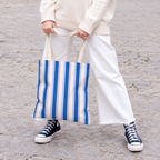 Model in white trousers carrying the Blue Cream Striped tote bag