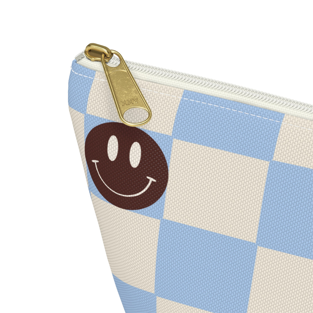 Close-up of the gold zipper pull on the blue smiley face checkered makeup bag