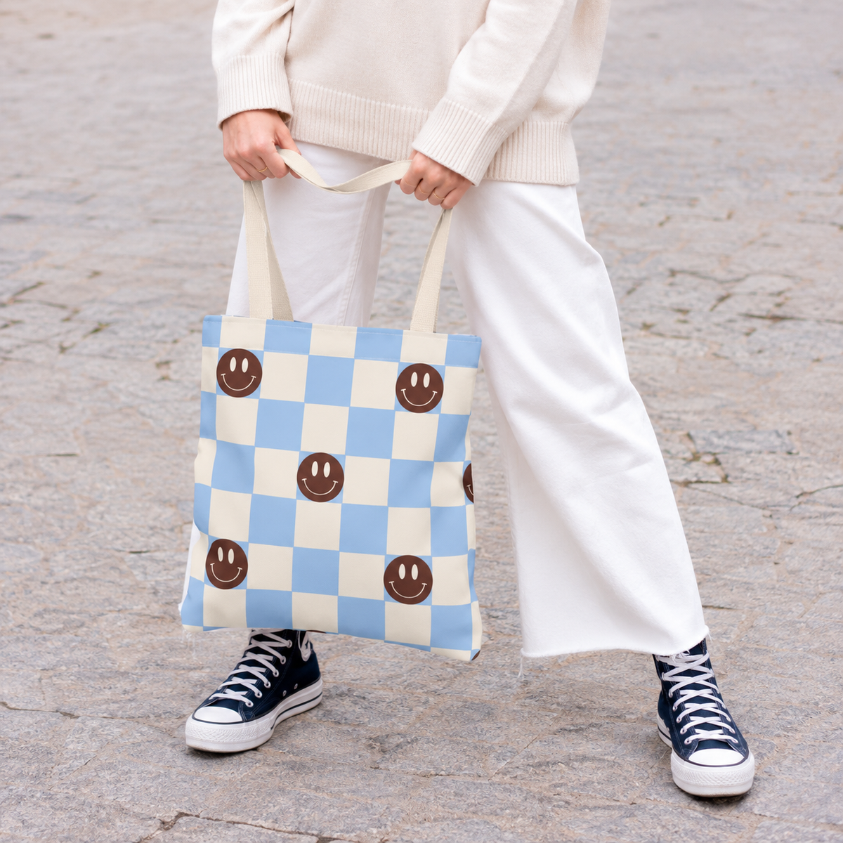 Woman holding the blue smiley face checkered tote bag in front of her on a street