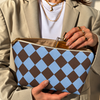 Hands opening a brown blue diamond checkered makeup bag filled with cosmetics