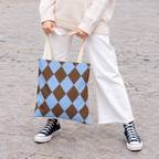 Woman holding a brown blue diamond checkered tote bag with white trousers and sneakers