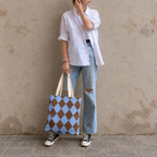 Woman leaning on a wall holding a brown blue diamond checkered tote bag