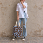 Woman leaning on a wall with a brown blue giraffe print tote bag
