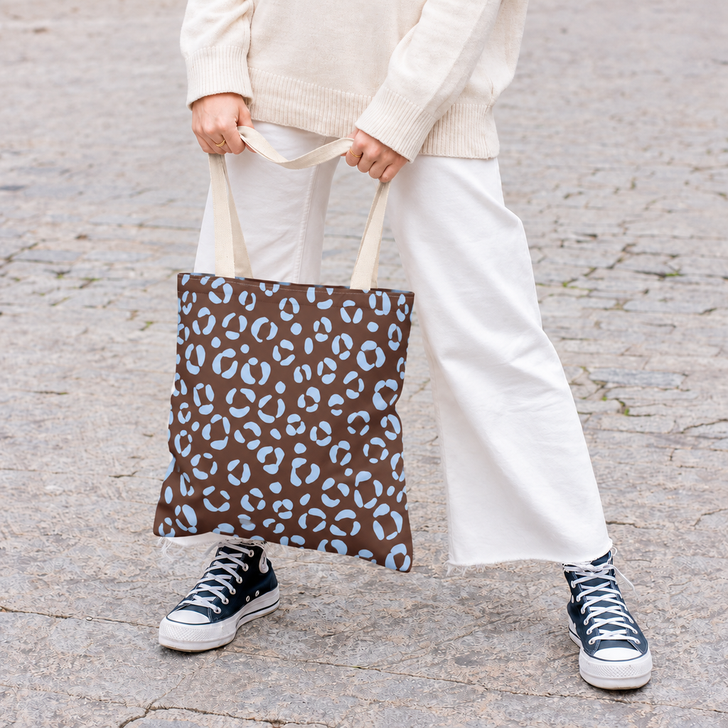 Woman holding a brown blue leopard print tote bag with white trousers and sneakers