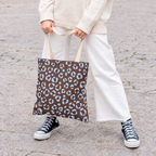 Woman holding a brown blue leopard print tote bag with white trousers and sneakers