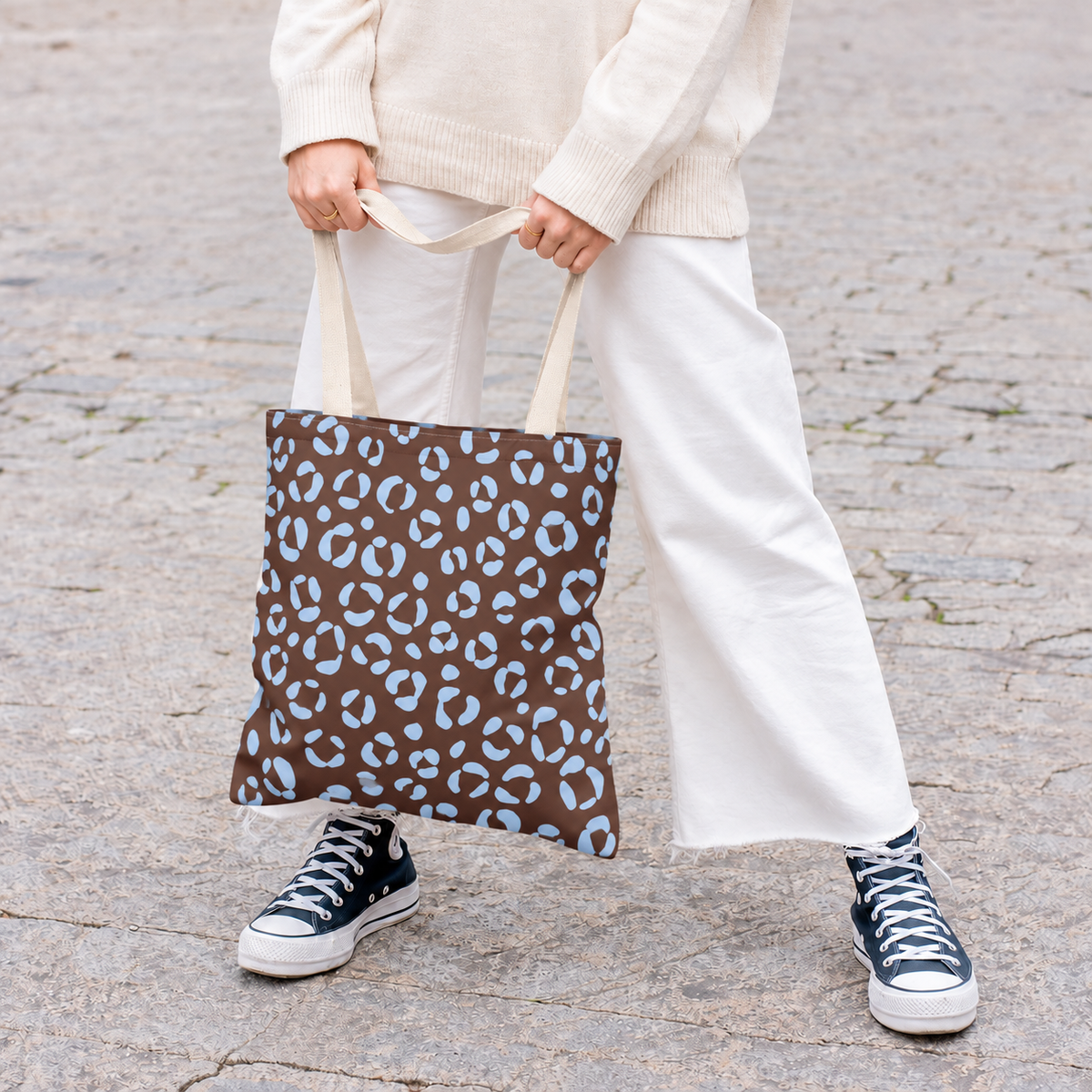 Woman holding a brown blue leopard print tote bag with white trousers and sneakers