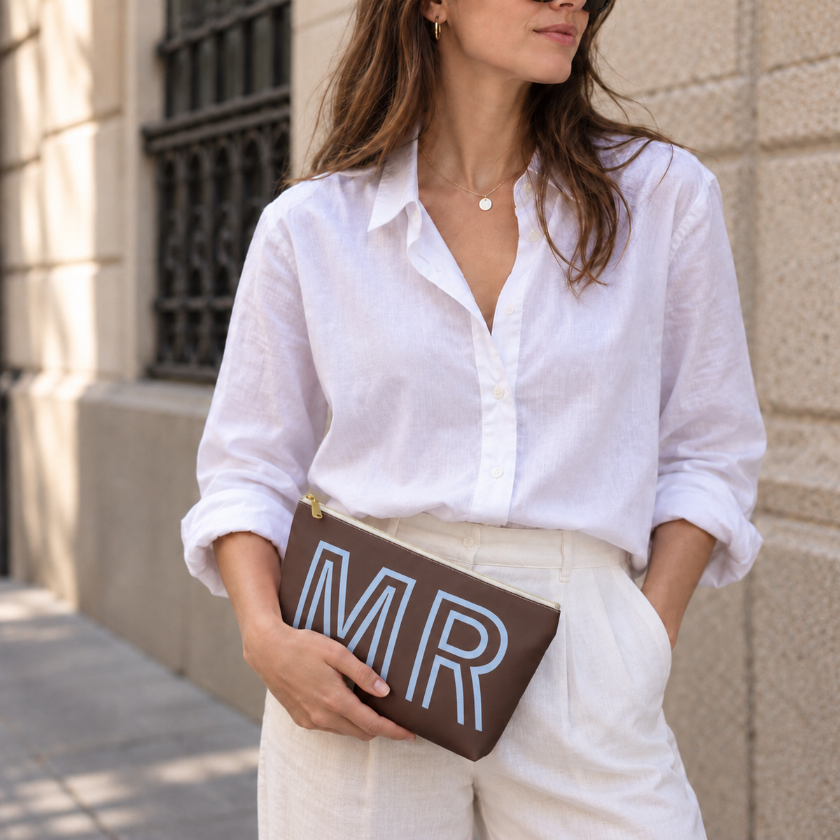 Woman in a white shirt holding the brown MR personalized makeup bag as a clutch
