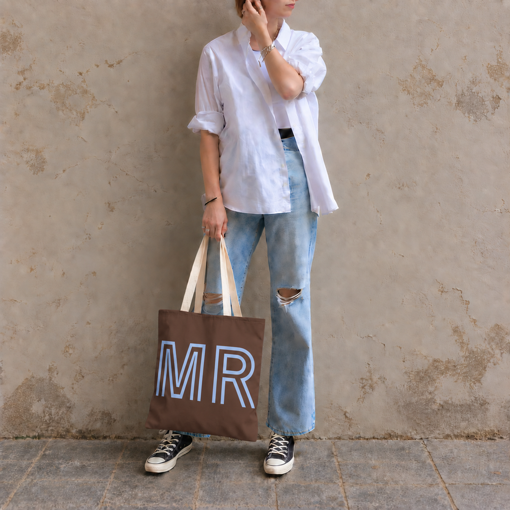 Woman in a white shirt and jeans holding the brown blue monogram personalized tote bag