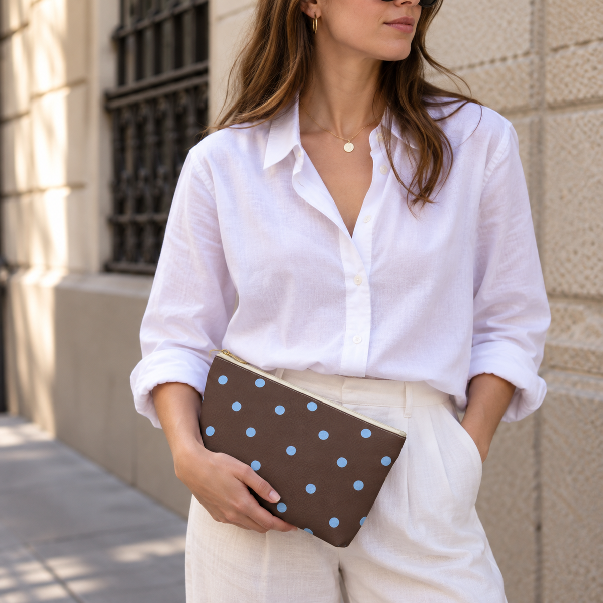 Woman in a white shirt holding the brown polka dot makeup bag at her hip