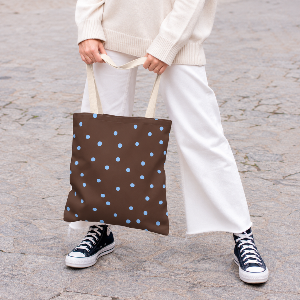 Woman holding the brown polka dot tote bag with blue dots in front of her on a street