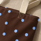 Close-up of the blue polka dots, stitching and cream handle of the brown tote bag