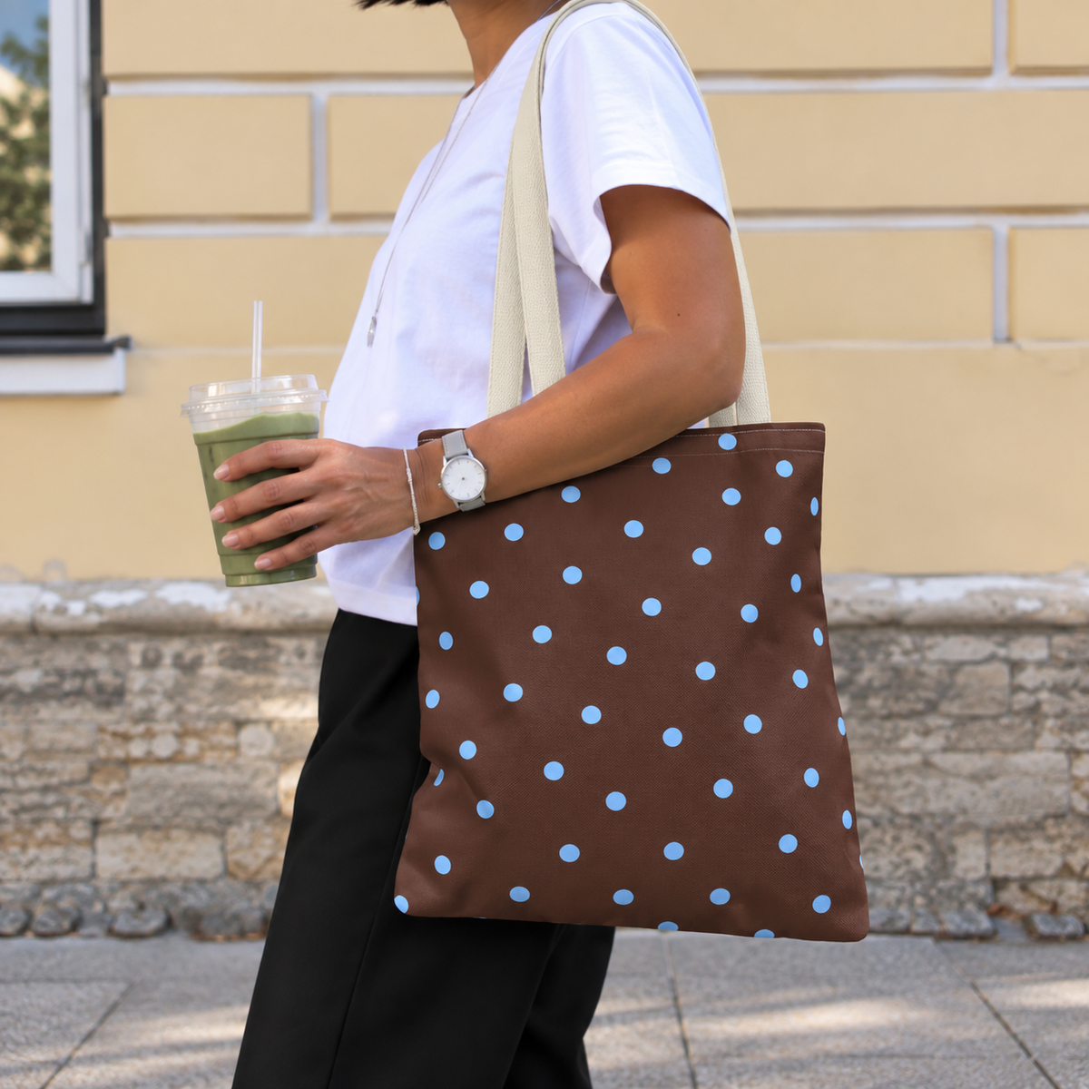 Side view of a woman wearing the brown blue polka dot tote bag on her shoulder