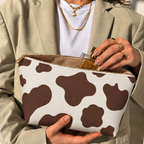Woman opening the brown cow print makeup bag to take out a perfume bottle
