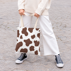 Woman holding the brown and white cow print tote bag in front of her on a street