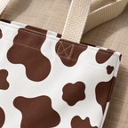 Close-up of the brown cow print patches and cream handle of the tote bag