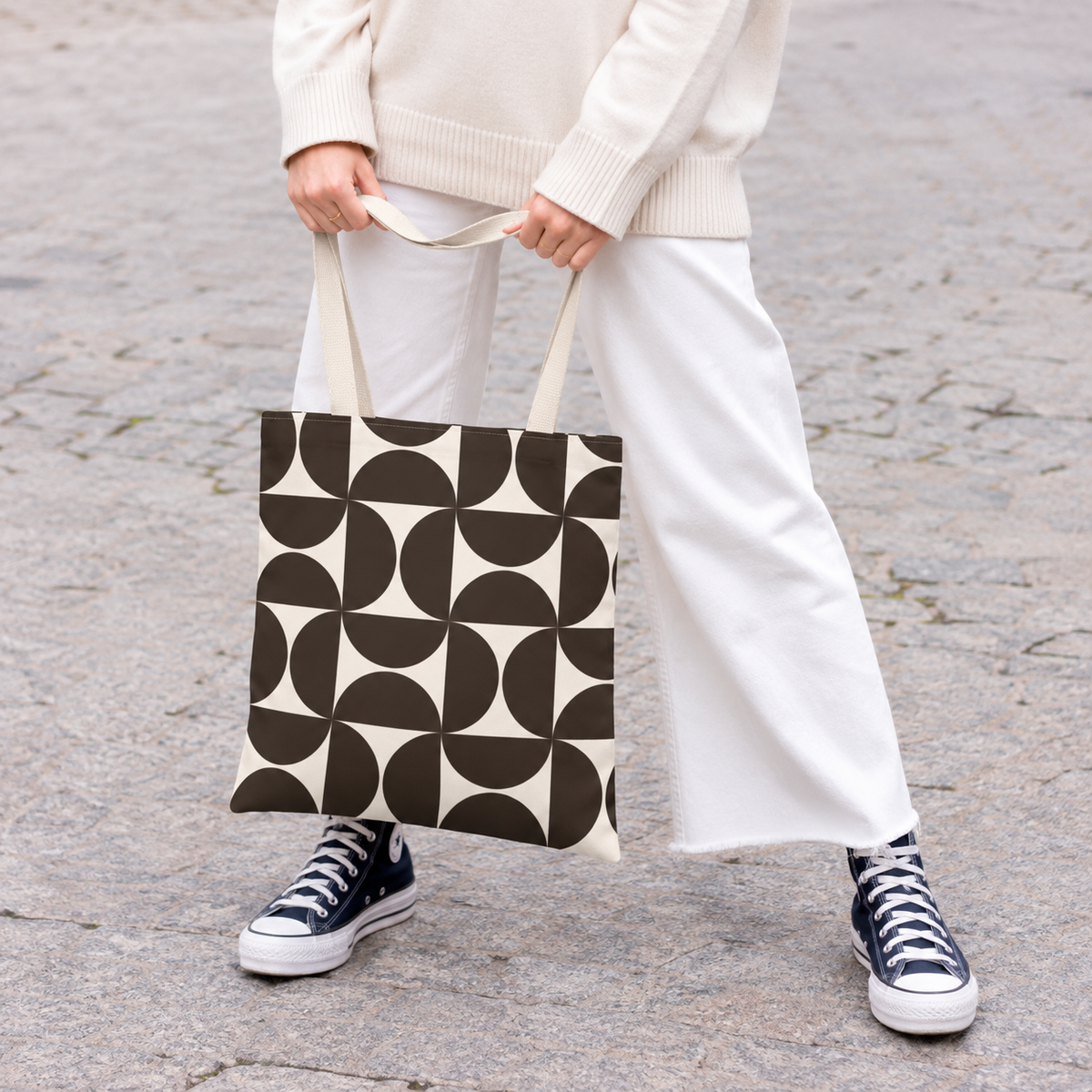 Woman in white trousers holding the brown cream geometric tote bag by the handles