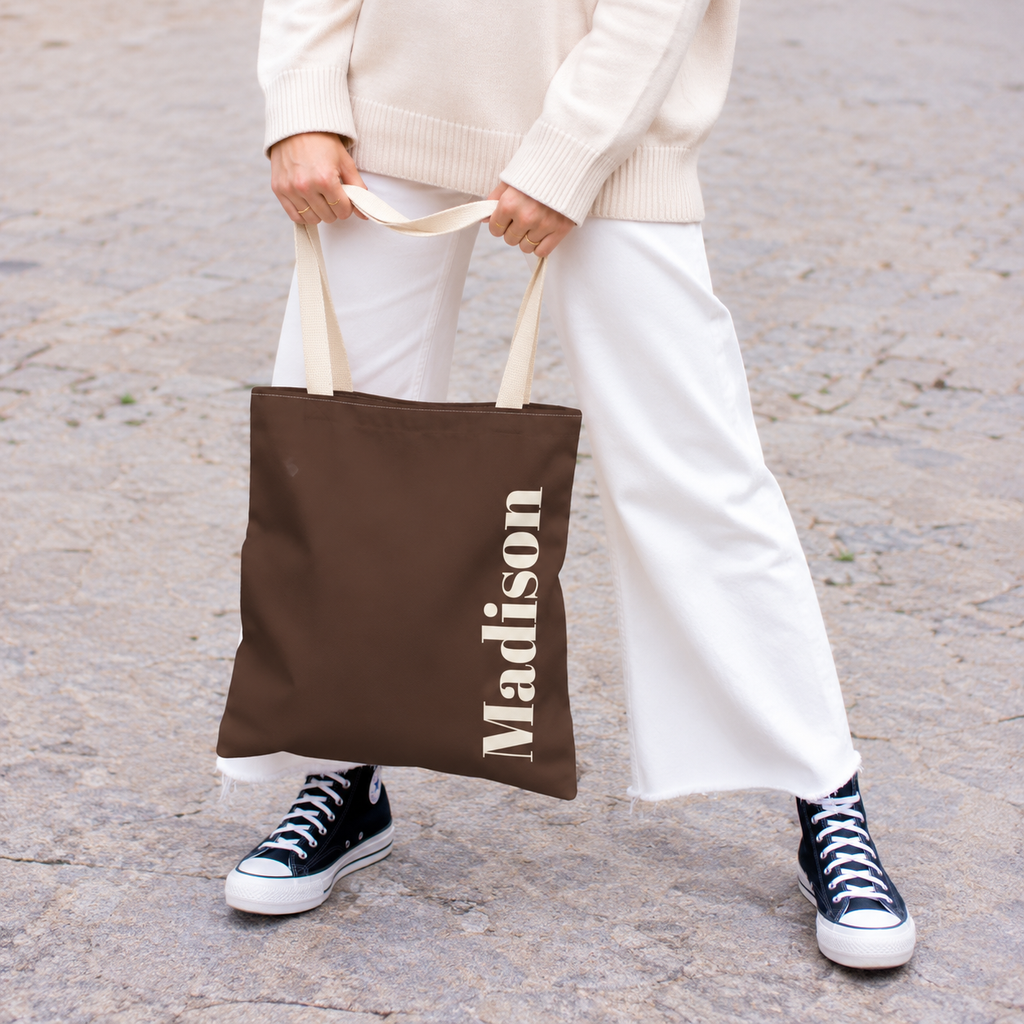 Model holding the Brown Cream Name personalized tote bag in front of white trousers