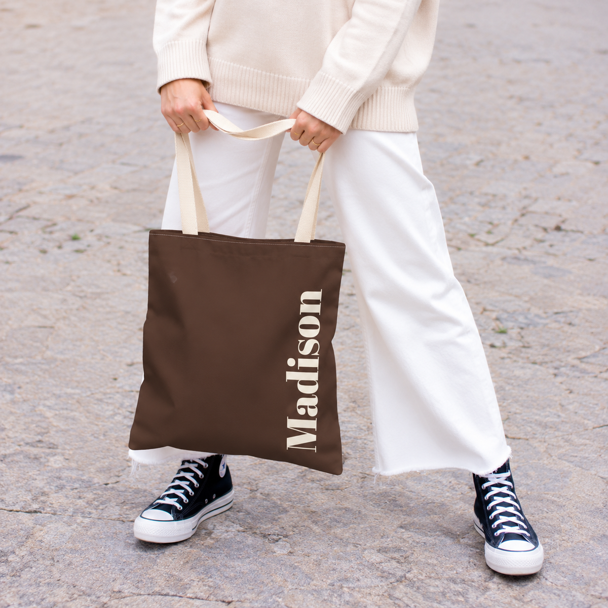 Model holding the Brown Cream Name personalized tote bag in front of white trousers