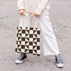 Woman in white trousers holding the brown cream triangle tote bag by the handles