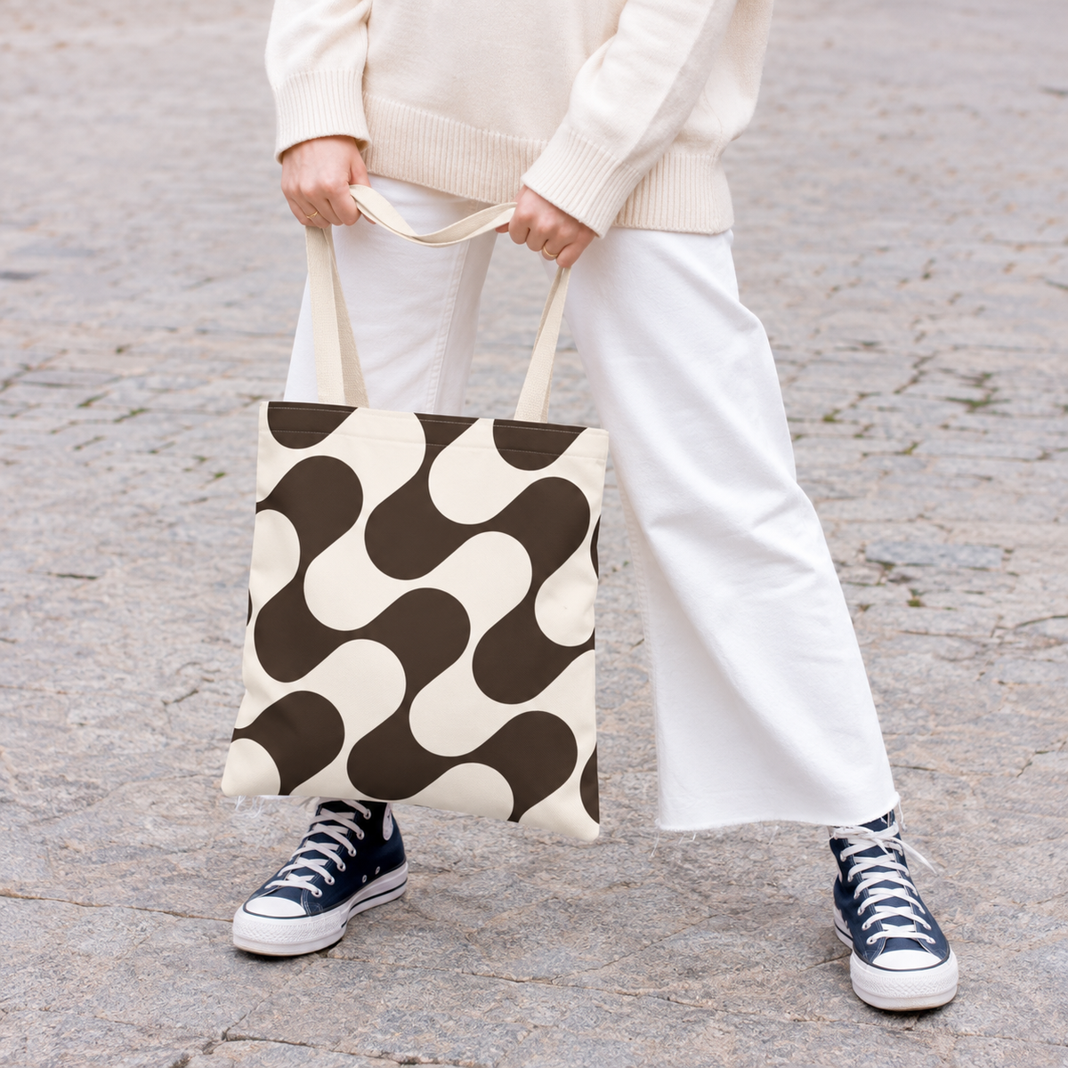 Woman in white trousers holding the brown cream wave tote bag by the handles