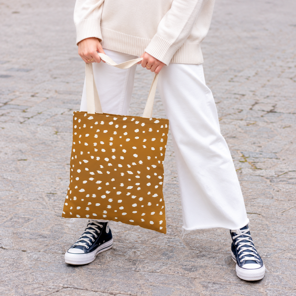 Model holding the Brown Fawn Spotted tote bag in front of white trousers